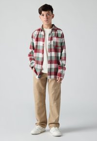 Πλαϊνό πουκάμισο καρό σε κόκκινο, πράσινο και λευκό, με κουμπιά και τσέπη; συνδυασμένο με μπεζ παντελόνια cargo και λευκά sneakers.