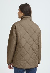 Brown, quilted jacket with a high collar, featuring a diamond pattern and black accents, seen from the back. Textured fabric.