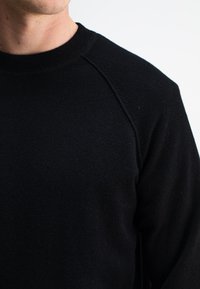 Schwarzer Fleece-Sweatshirt mit geripptem Rundhalsausschnitt und Raglanärmeln. Der Stoff ist weich und hat eine strukturierte Oberfläche, ohne sichtbare Muster oder Akzentuierungen.