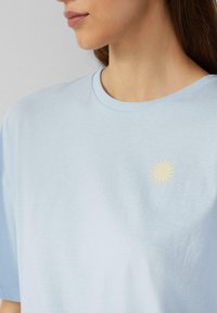 Lichtblauwe korte mouwen T-shirt van katoen, met een kleine gele zonafbeelding op de linkerborst. Zachte textuur, ronde hals.