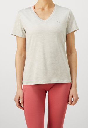 Frau trägt ein hellgraues kurzärmeliges V-Ausschnitt-Shirt und korallenfarbene Leggings, steht vor einem schlichten weißen Hintergrund.