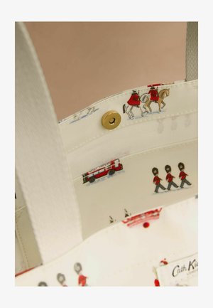 Lõuendist käekoti sisu, kreemikat värvi, millel on printitud mustris valvurid, hobused ja tuletõrjeauto. Kuldse kinnituse detail kinnitub klõpsuga.