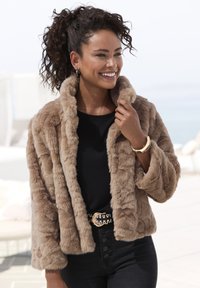 Svetlo rjav plašč iz umetnega krzna z puhasto teksturo, širokim ovratnikom in dolgimi rokavi. Nosen čez črn top in v kombinaciji s temnimi kavbojkami.