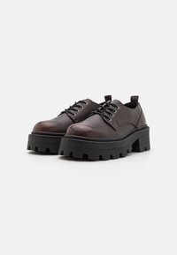 Scarpe stringate in pelle marrone con punta rotonda e suola piattaforma nera spessa caratterizzata da una texture robusta e seghettata.
