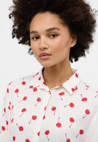 White shirt with red cherry patterns, featuring a classic collar and buttons. Soft fabric with a smooth texture.