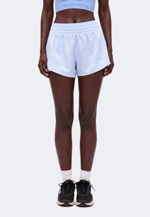 Personne portant un short Nike Pro bleu clair et un soutien-gorge de sport, des chaussettes blanches aux chevilles et des chaussures de course noires, debout les pieds joints.