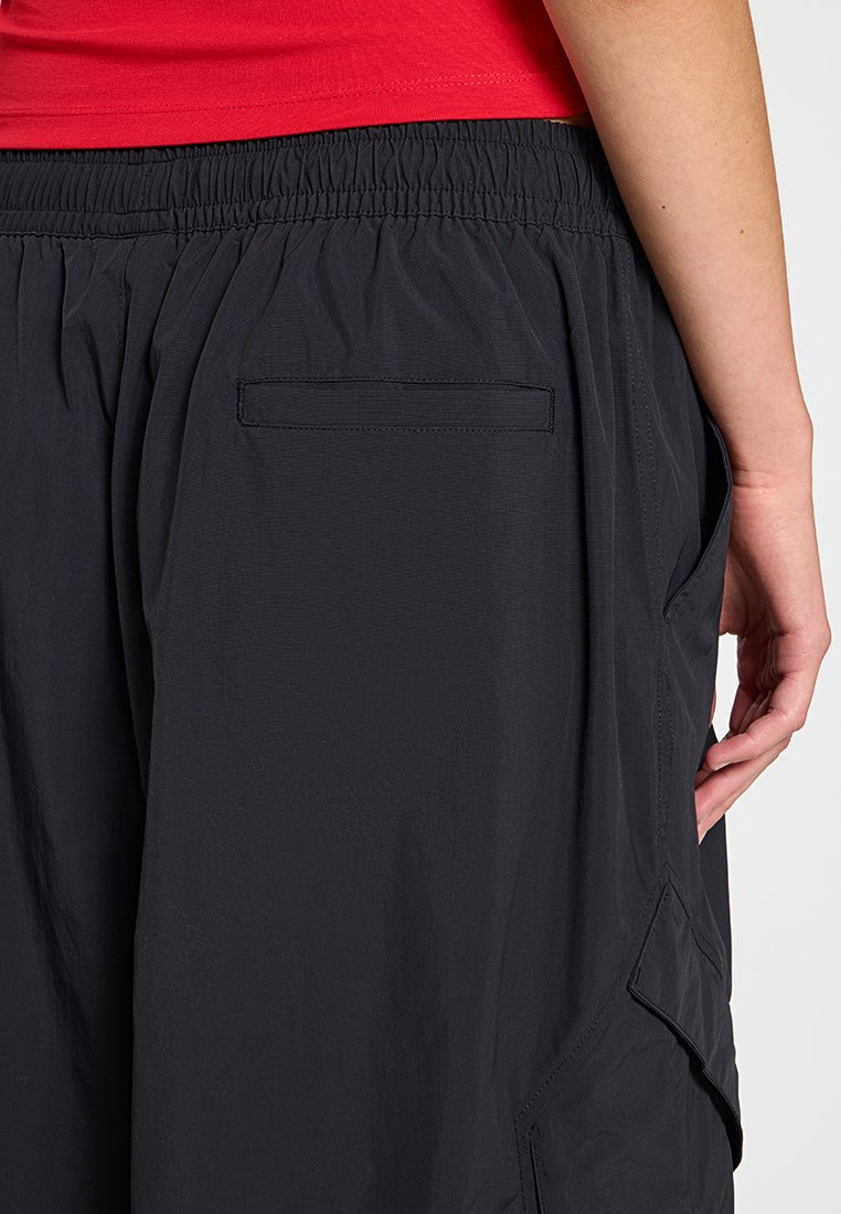 Pantaloni corti neri leggeri con cinturino elastico, dotati di tasca sul retro e tasca laterale cargo, texture liscia e vestibilità rilassata.