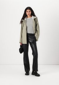 Veste vert olive avec capuche, pantalon en faux cuir noir et haut à rayures blanches. Les accessoires comprennent un sac à main noir et des chaussures noires.
