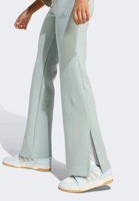 Jasnozielone dresy z bocznymi rozporkami, wykonane z miękkiego materiału, zestawione z jasnoniebieskimi sneakersami z białymi paskami i beżowymi podeszwami.