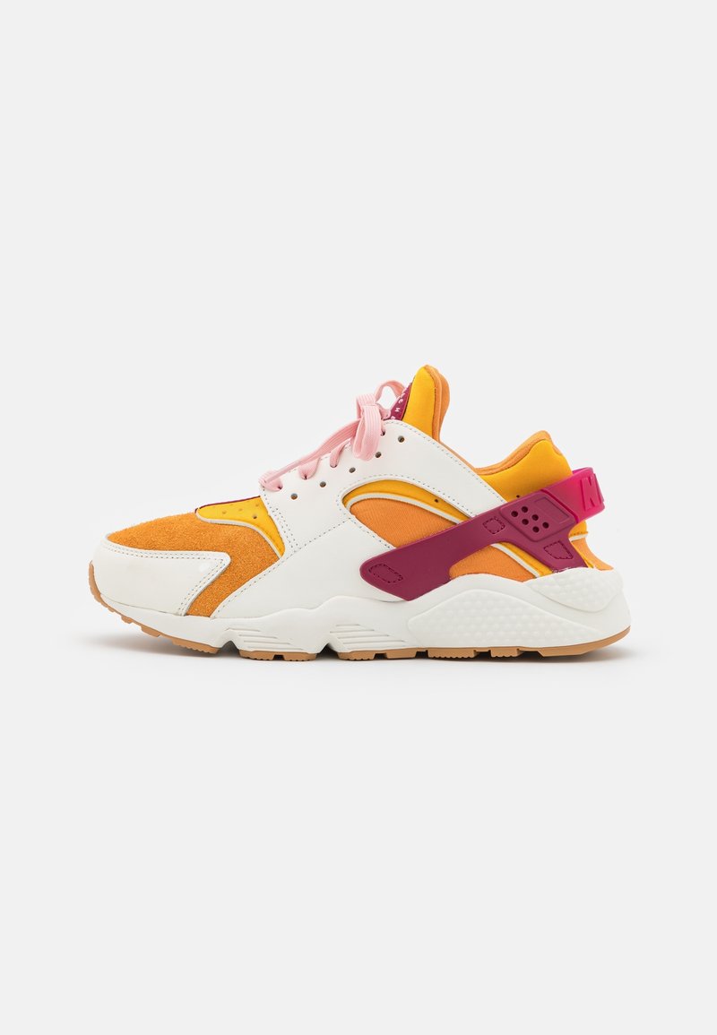 Låg sneaker med vita, orange och gula paneler, rosa snören och en rosa hälrem mot en enfärgad vit bakgrund.