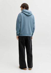 Felpa con cappuccio morbida e blu con tasca a marsupio e cappuccio con coulisse regolabile, abbinata a pantaloni di jeans neri a taglio ampio.