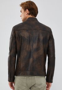 Bruine versleten leren jas met een klassieke kraag, lange mouwen en zichtbare stiksels. Het oppervlak heeft een gestructureerde afwerking.