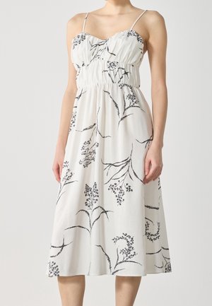 Weißes knielanges Kleid mit dünnen Trägern, das eine geraffte Taille und einen floralen Druck in Schwarz hat, aus leichtem Stoff gefertigt.