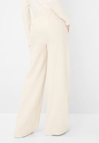 Beige, weite Hose mit strukturiertem Finish, mit einem elastischen Bund und zwei Gesäßtaschen, von hinten gezeigt.