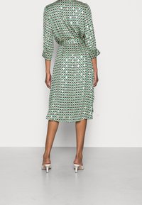 Abito verde con un motivo geometrico a triangolo in blu e blu navy, con vita accentuata da una cintura, maniche a tre quarti e lunghezza midi.