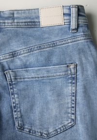 Světle modré džíny z denimu s jednou zadní kapsou a koženou etiketou s vyraženým textem. Tkanina má jemnou strukturu s mírným vyblednutím.