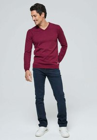 Pull à col en v bordeaux en tissu tricoté, associé à un jean bleu foncé et des baskets blanches, présentant une coupe décontractée et une texture douce.