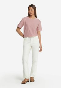 Ljusrosa t-shirt med kort ärm, kombinerad med vita raka jeans och bruna sandaler. Enkla linjer med rund nacke och avslappnad passform.