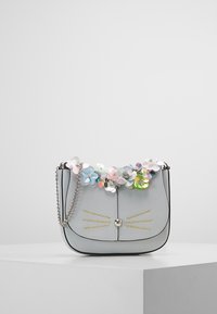 Šedá kožená crossbody taška s květinovými ozdobami, řetízkovým popruhem a detaily připomínajícími vousky. Má hladkou texturu a zaoblený tvar.