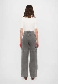 Grå høy midje cargo bukser med vide ben, flere lommer foran og bak, sømdetaljer og et teksturert denimstoff.