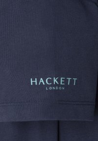 Tamsiai mėlynas marškinėliai, pagaminti iš minkštos medvilnės, su apvalia iškirpte ir trumpomis rankovėmis, su šviesiai mėlynu „HACKETT LONDON“ logotipu.