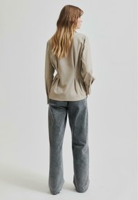 Beige langermet skjorte med avslappet passform og knappemanchetter, paret med vide grå bukser i et mykt, teksturert stoff.
