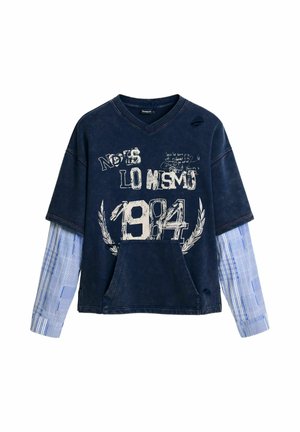 Felpa oversize blu navy con maniche corte, tasca frontale, testo grafico, dettagli consumati e una camicia a maniche lunghe a quadri a contrasto sotto.