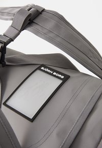 Saco de duffel cinza com tecido texturizado, alças ajustáveis e um rótulo preto com a inscrição "BJÖRN BORG." Seção em plástico transparente para identificação.
