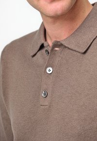 Braun gestricktes Poloshirt mit Knopfleiste, ausgestattet mit drei Knöpfen, einem strukturierten Kragen und einem kleinen Ausschnittdetail in der Nähe des Ausschnitts.