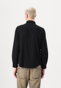Black long-sleeve shirt with a curved hem and button cuffs, made from cotton fabric. Features a simple collar and a solid color design.
