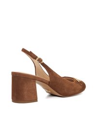 Bruine suède slingback schoen met een ronde neus, chunky hak en gouden hardware detail. Heeft een gladde textuur en open zijkanten.