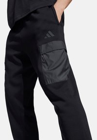 Schwarze Cargo-Hose mit schlankem Design, aus weichem Stoff gefertigt, mit einer markanten glatten Taschenseite und dezentem Logodetail.