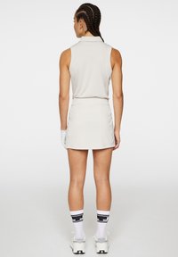 Hihaton, vaalea beige polo-paita kauluksella, yhdistettynä matching-hameeseen. Mallilla on valkoiset sukat mustilla yksityiskohdilla ja tennarit.