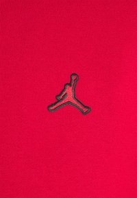 Tessuto rosso con una texture a coste presenta un logo Jumpman nero ricamato al centro del petto.
