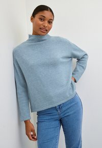 Maglione azzurro chiaro con collo alto, realizzato in tessuto morbido, dotato di maniche lunghe e vestibilità rilassata, abbinato a jeans blu.