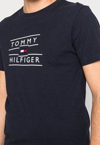 Marineblå bomulds T-shirt med hvid "TOMMY HILFIGER" tekst og et lille broderet logo i rød, hvid og blå på brystet.