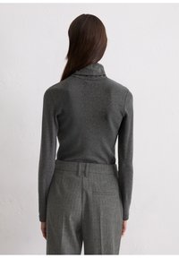 Graues langärmliges Oberteil mit hohem Kragen aus weichem Stoff, kombiniert mit grauen Nadelstreifen-Hosen, die eine Gesäßtasche und Gürtelschlaufen aufweisen.