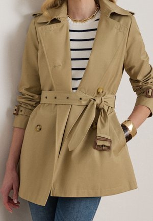 Beige trenchcoat med bælte over stribet sweater, med guldkædehalskæde og guldfarvede og skildpaddearmbånd på håndleddet.