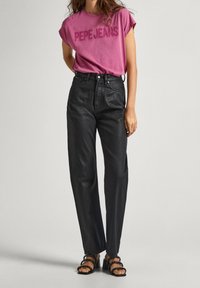 Rosa t-shirt med texten "PEPE JEANS", kombinerad med högmidjade svarta jeans. Sandalerna har en flerbandsdesign och blockklackar.