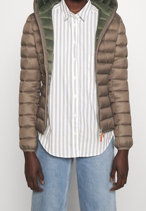 Person trägt eine hellbraune Steppjacke mit olivgrünem Futter, ein gestreiftes weiß-beiges Hemd mit Knöpfen und eine hellblaue Jeans.