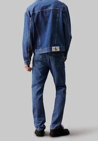 Jeansová bunda a džíny v středně modré barvě, s výraznou zadní etiketou. Jednoduchý design s volným střihem a minimem kovových detailů.