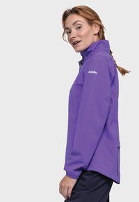 Leichte lila Jacke mit Reißverschluss, hohem Kragen und elastischen Bündchen. Mit einem Logo auf der Schulter und seitlichen Taschen.