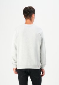 Grey sweatshirt with long sleeves, crew neck, and slightly textured fabric. Features a small brand logo near the bottom hem.