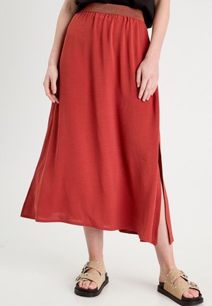 Rødt maksinederdel med tekstureret, elastisk talje og sideslids; kombineret med beige sandaler med dekorative detaljer og nitter.