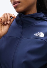 Ναυτικό μπουφάν με φερμουάρ και κουκούλα, με το λογότυπο The North Face σε λευκό χρώμα. Λεπτό και απαλό ύφασμα με καλοσχηματισμένη εφαρμογή και προσεγμένες ραφές.