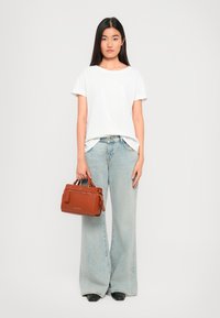Chemise blanche à manches courtes, jean large bleu clair, chaussures noires et un petit sac à main marron avec des zips et une poignée supérieure.