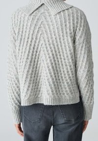 Pull épais en maille torsadée gris clair avec un col côtelé haut, porté avec un jean gris foncé, vu de dos.