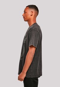 Black cotton t-shirt with a relaxed fit, rolled sleeves, faded texture, and a circular graphic printed in gray on the front.