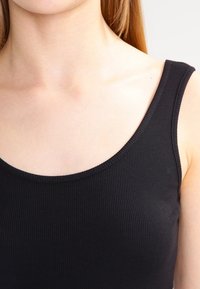 Czarny prążkowany top na ramiączkach z okrągłym dekoltem i szerokimi ramiączkami. Miękka tekstura i dopasowany krój, idealny do warstwowania lub na co dzień.