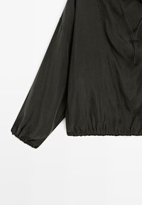Schwarze, leichte Pulloverjacke mit langen, elastischen Ärmeln und Kapuze mit Kordelzug. Verfügt über ein gefälteltes Design und einen gerafften Bund.